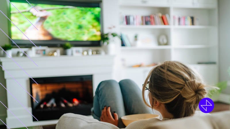 blonde woman with glasses watching tv on a couch with a snack in a porcelain bowl